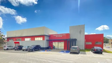 Fachada da Câmara Municipal de Potim em São Paulo, apresentando um edifício moderno de linhas retas nas cores cinza e vermelho, com estacionamento frontal e céu azul ao fundo. Foto: Divulgação/Câmara Municipal de Potim-SP