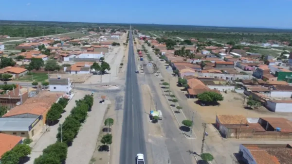 Vista aérea de Campo Grande do Piauí, mostrando uma rodovia asfaltada que corta a cidade em linha reta sob um céu azul. Dos dois lados da estrada, há casas de telhado cerâmico, ruas de terra e árvores baixas. Ao fundo, a paisagem é dominada por uma vasta área de vegetação rasteira e horizonte plano.