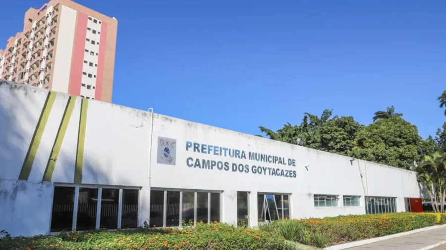Fachada do prédio da Prefeitura Municipal de Campos dos Goytacazes com jardim florido à frente e prédio residencial ao fundo sob céu azul. Foto: Divulgação/Prefeitura de Campos dos Goytacazes-RJ