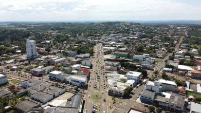 Vista aérea da cidade de Capanema-PR com avenida central, prédios comerciais, residenciais e área verde ao fundo. Foto: Divulgação/Prefeitura de Capanema-PR