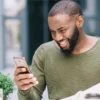 Homem sorridente segurando celular e jornal enquanto está sentado ao ar livre. Foto: Freepik