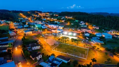 Vista aérea noturna de uma cidade pequena com casas iluminadas, ruas arborizadas e um campo esportivo central cercado por postes de luz. Foto: Divulgação/Prefeitura de Capitão-RS