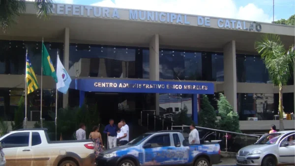 Fachada da Prefeitura Municipal de Catalão com entrada principal, bandeiras hasteadas e pessoas circulando em frente ao prédio.