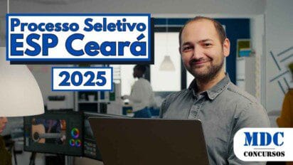 Homem sorridente com barba rala e cabelo curto segura um notebook prateado em um escritório moderno e bem iluminado, usando camisa cinza de botão. Ao fundo, outras pessoas trabalham em mesas com computadores e prateleiras com materiais organizados. A decoração do ambiente é contemporânea, com paredes em azul e branco, luminárias pendentes e janelas grandes que permitem entrada de luz natural - Ceará abre 7 Vagas + CR com salários de até R$ 7 mil em Processo Seletivo na ESP/CE