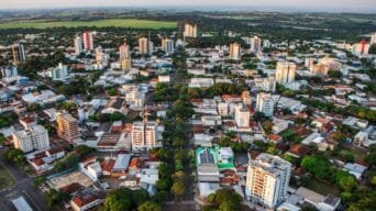 Vista aérea da cidade de Cianorte-PR com prédios, ruas arborizadas e área verde ao fundo.