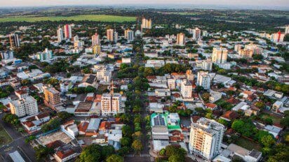 Vista aérea da cidade de Cianorte-PR com prédios, ruas arborizadas e área verde ao fundo.