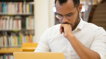 Homem de óculos concentrado usando notebook em biblioteca. Foto: pch.vector/Freepik