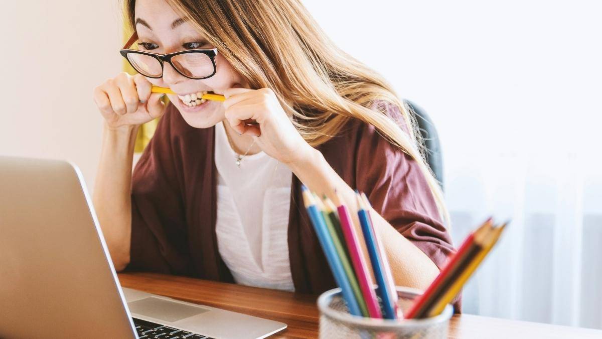 Como montar um plano de estudos do zero: guia prático para iniciantes 1 Como montar um plano de estudos do zero: Mulher de óculos, com o cabelo comprido, vestindo um casaco marrom, mordendo um lápis enquanto olha para a tela de um notebook. Foto: jeshoots/Unsplash