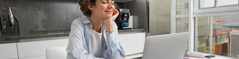 SEMED Monte Negro-RO lança processo seletivo p/ Professores 2 Mulher sorridente sentada à mesa usando notebook em ambiente doméstico iluminado.