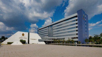 Prédio da Assembleia Legislativa do Estado do Amazonas com fachada moderna, área externa ampla e céu parcialmente nublado ao fundo.