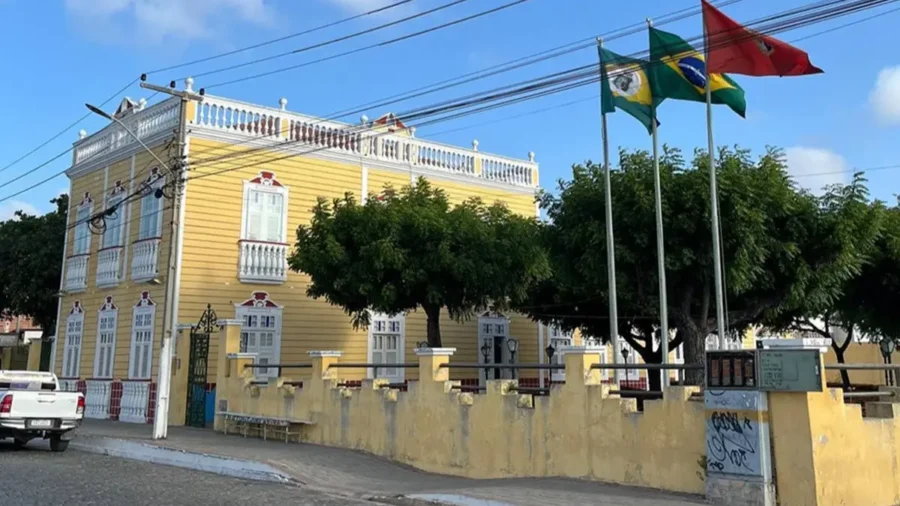 Fachada amarela da Prefeitura Municipal de Aracati com bandeiras ao vento, sede do concurso Aracati CE