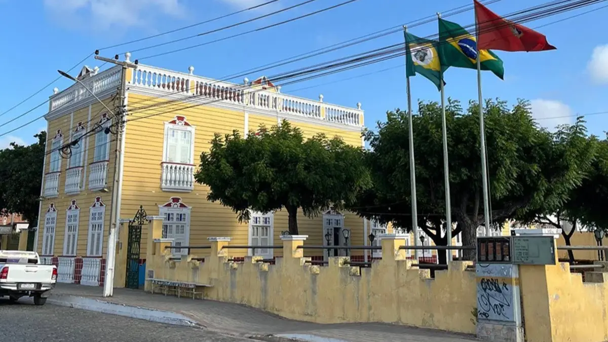 Fachada amarela da Prefeitura Municipal de Aracati com bandeiras ao vento, sede do concurso Aracati CE