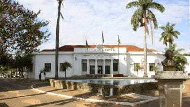 Prédio da Prefeitura Municipal de Birigui-SP com fonte, bandeiras e busto em praça arborizada. Foto: Divulgação/Prefeitura de Birigui-SP