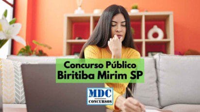 Mulher jovem com expressão pensativa sentada em sofá, usando blusa amarela e olhando para um notebook, enquanto segura uma caneta e faz anotações. Ao fundo, há uma estante com objetos decorativos em ambiente doméstico. Sobre a imagem, há um banner verde com os dizeres “Concurso Público Biritiba Mirim SP” e o logotipo da MDC Concursos na parte inferior.