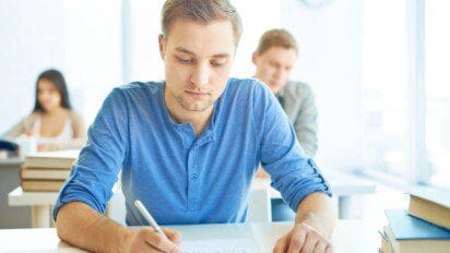 Jovem escrevendo em prova dentro de sala de aula, com outros estudantes ao fundo. Foto: pressfoto/Freepik