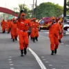 Bombeiros militares em uniforme laranja e banda desfilam em rua, concurso CBMMA