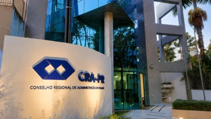 Placa com logotipo do CRA-PR na entrada do prédio de vidro, sede do concurso CRA PR