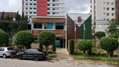 Concursos 5 Fachada da Câmara Municipal com placa e bandeiras ao fundo, referente ao concurso Câmara de João Monlevade MG
