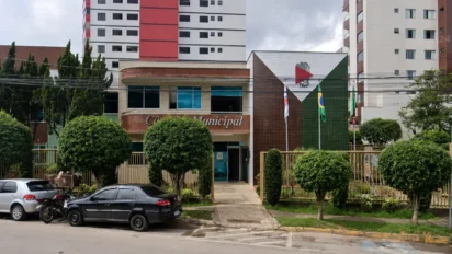 Fachada da Câmara Municipal com placa e bandeiras ao fundo, referente ao concurso Câmara de João Monlevade MG