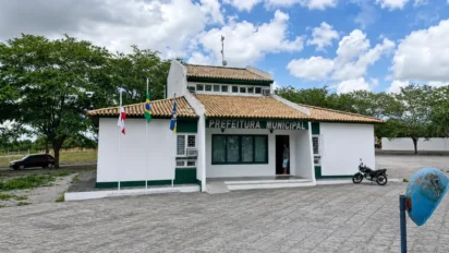 Prédio branco da prefeitura com três bandeiras e céu nublado, palco do concurso Conceição do Coité BA