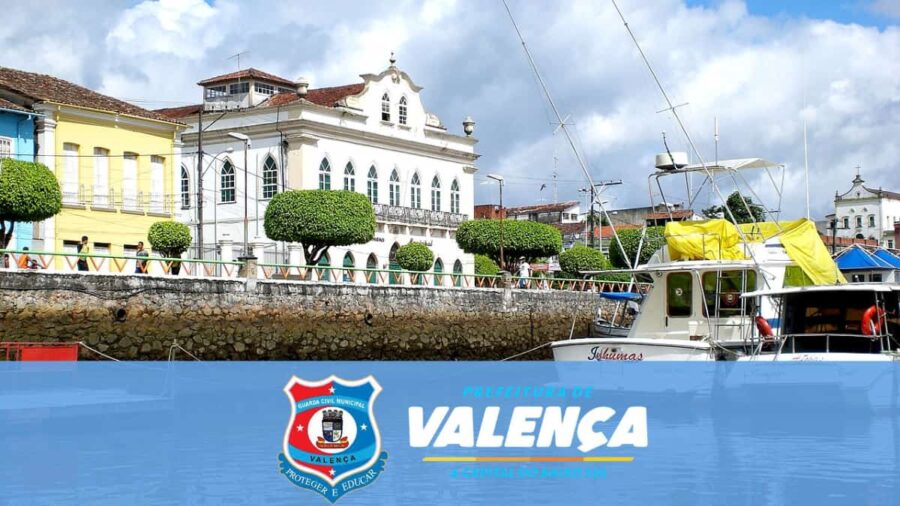 Vista do porto de Valença BA com barcos e prédios históricos ao fundo e o escudo da GCM no concurso GCM Valença BA