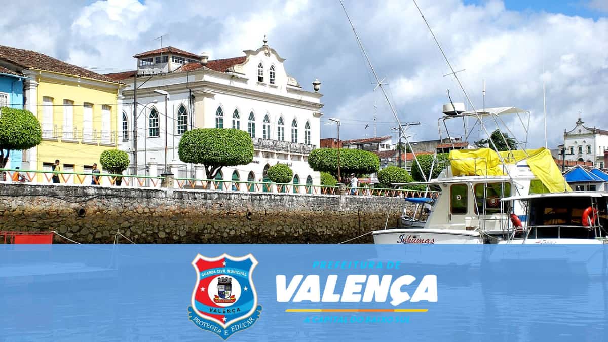 Vista do porto de Valença BA com barcos e prédios históricos ao fundo e o escudo da GCM no concurso GCM Valença BA