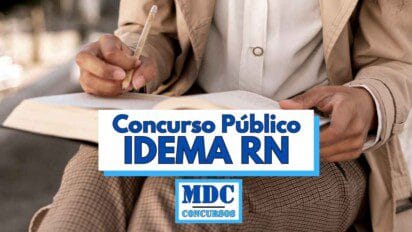 Pessoa segurando um caderno e escrevendo com um lápis, usando roupas sociais em tons claros, com a imagem focada nas mãos e no material de estudo; sobre a imagem há uma faixa branca e azul com o texto Concurso Público IDEMA RN em letras grandes e o logotipo da MDC Concursos logo abaixo