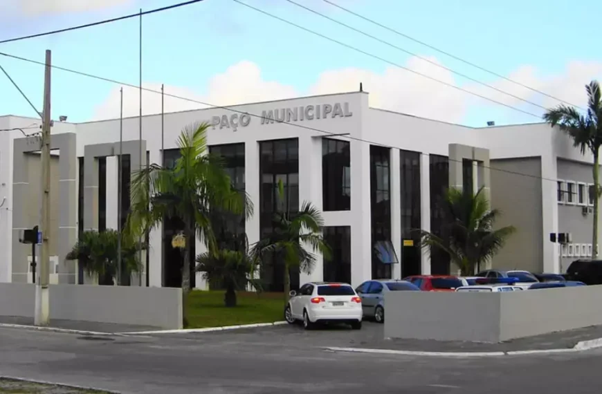 Fachada do Paço Municipal de Matinhos, sede da prefeitura responsável pelo concurso Matinhos PR, com palmeiras e estacionamento ao fundo