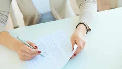 Pessoa preenchendo cartão de respostas de prova com caneta em uma mesa branca. Foto: pressfoto/Freepik