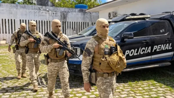 Policiais penais fardados com coletes táticos e fuzis ao lado de viatura do concurso PPRN