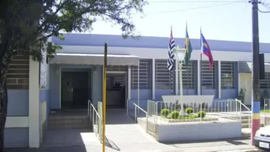 Fachada azul de prédio público com três bandeiras hasteadas, cenário do concurso Piraju SP
