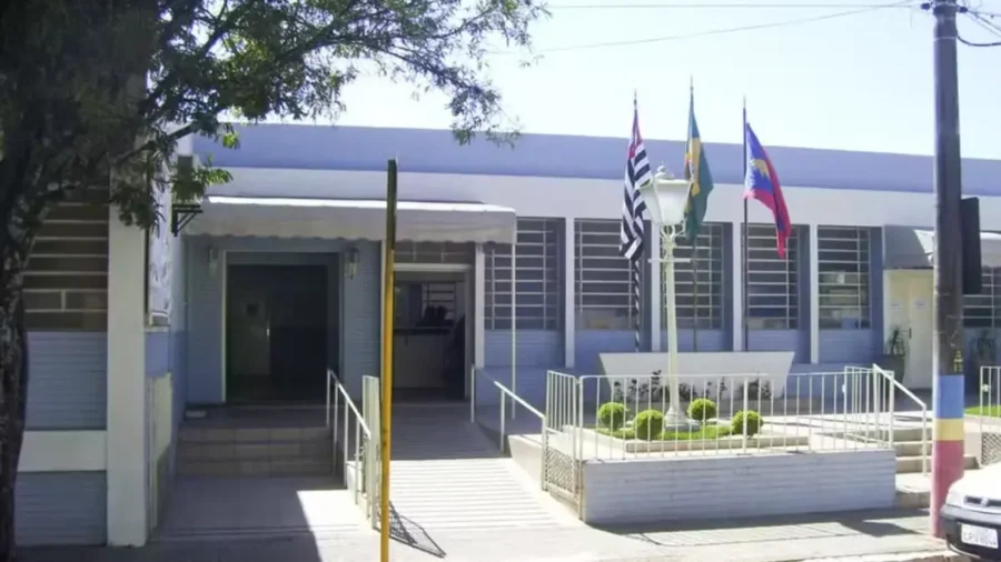 Fachada azul de prédio público com três bandeiras hasteadas, cenário do concurso Piraju SP