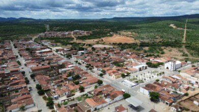Vista aérea da cidade de Riacho de Santo Antônio com casas de telhado vermelho, praça central e igreja cercadas por área verde e morros ao fundo. Foto: Divulgação/Prefeitura de Riacho de Santo Antônio-PB