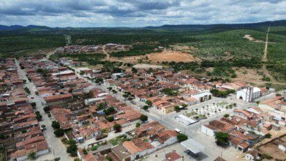 Vista aérea da cidade de Riacho de Santo Antônio com casas de telhado vermelho, praça central e igreja cercadas por área verde e morros ao fundo. Foto: Divulgação/Prefeitura de Riacho de Santo Antônio-PB