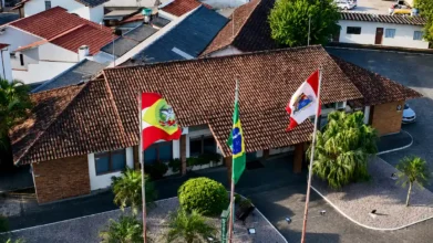 Vista aérea da sede da prefeitura com três bandeiras hasteadas, concurso Tijucas SC