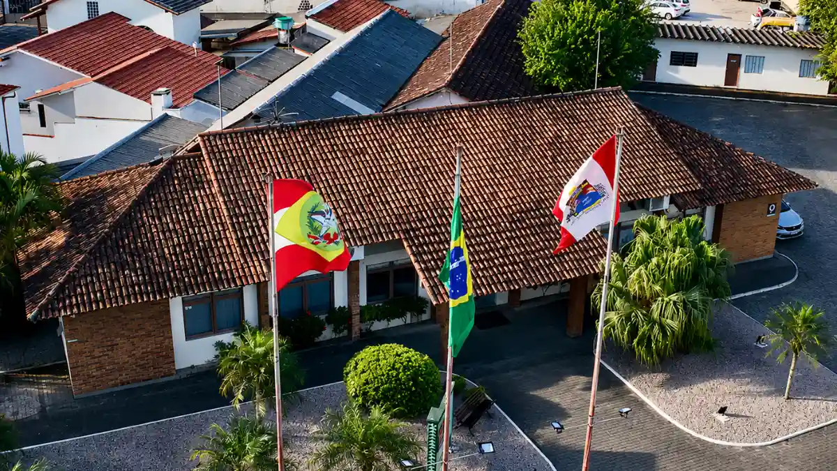 Vista aérea da sede da prefeitura com três bandeiras hasteadas, concurso Tijucas SC