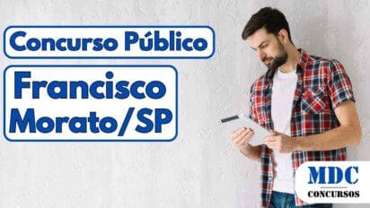 Homem de barba usando camisa xadrez vermelha sobre camiseta branca, segurando e olhando para um tablet em frente a uma parede branca texturizada - Concurso em Francisco Morato (SP) oferece 26 vagas e salários de até R$ 7.159,78