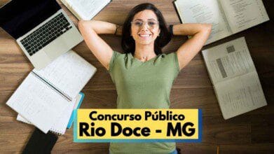 Mulher jovem de óculos e camiseta verde sorri deitada no chão com as mãos atrás da cabeça, em meio a cadernos, livros abertos e um notebook, simbolizando preparação para concurso público. Na parte inferior da imagem, há uma faixa com os dizeres “Concurso Público Rio Doce – MG”, indicando que se trata de uma divulgação de concurso público municipal.
