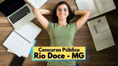 Mulher jovem de óculos e camiseta verde sorri deitada no chão com as mãos atrás da cabeça, em meio a cadernos, livros abertos e um notebook, simbolizando preparação para concurso público. Na parte inferior da imagem, há uma faixa com os dizeres “Concurso Público Rio Doce – MG”, indicando que se trata de uma divulgação de concurso público municipal.