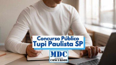 A imagem mostra um homem vestindo uma blusa branca de manga comprida, sentado à mesa, estudando. Ela está com um caderno aberto, segurando uma caneta em uma mão e digitando em um notebook com a outra. Em destaque, há uma faixa com os dizeres “Concurso Público Tupi Paulista SP” e o logotipo da “MDC Concursos” na parte inferior central da imagem. A cena transmite um ambiente de estudo e preparação para concursos públicos.