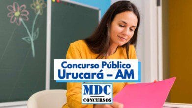 Imagem colorida de uma mulher com cabelos castanhos, usando blusa amarela, sentada em uma sala de aula, segurando uma pasta rosa. Ao fundo, há um quadro verde com desenhos de flores e uma parede azul. Em destaque no centro da imagem, há um banner com os dizeres “Concurso Público Urucará – AM” e a logomarca “MDC Concursos” logo abaixo. A cena transmite um ambiente educacional acolhedor e informativo.