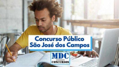 Homem jovem de pele parda e cabelo crespo preso em um coque estuda concentrado em um ambiente iluminado, com livros e caderno abertos sobre a mesa. Ele segura um lápis com a mão direita e está voltado para um notebook. No centro da imagem há um banner com os dizeres “Concurso Público São José dos Campos” e o logotipo “MDC Concursos” abaixo.