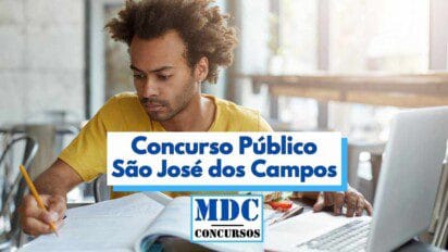 Homem jovem de pele parda e cabelo crespo preso em um coque estuda concentrado em um ambiente iluminado, com livros e caderno abertos sobre a mesa. Ele segura um lápis com a mão direita e está voltado para um notebook. No centro da imagem há um banner com os dizeres “Concurso Público São José dos Campos” e o logotipo “MDC Concursos” abaixo.