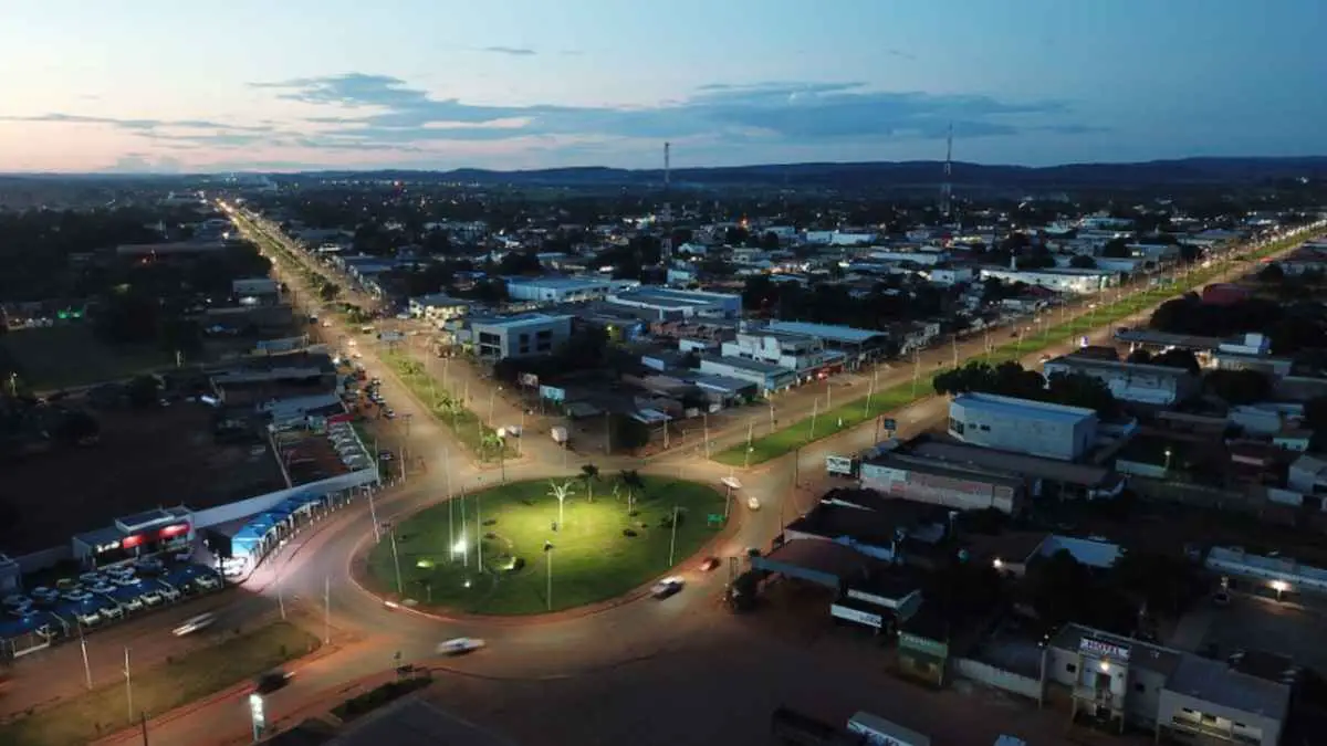 Vista aérea de uma rotatória iluminada ao entardecer na cidade de Confresa, MT, com avenidas extensas e prédios comerciais ao redor.