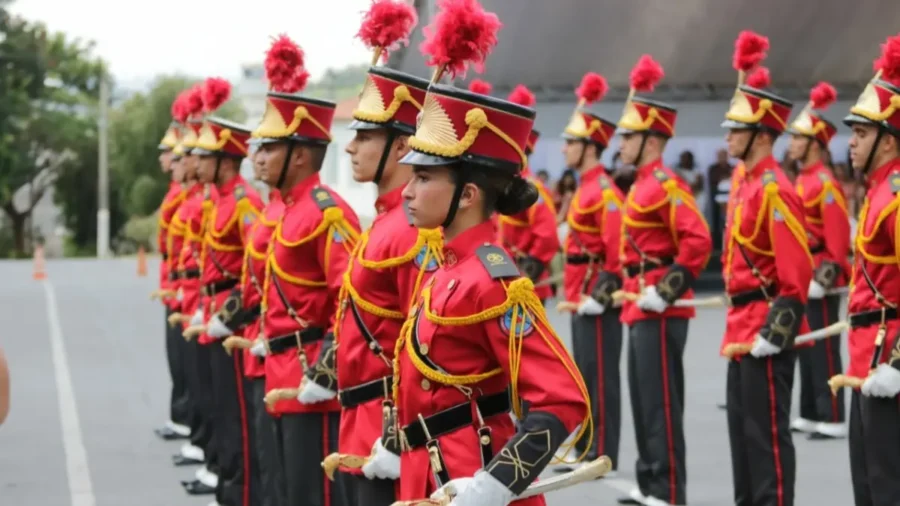 Cadetes do Corpo de Bombeiros de Minas Gerais perfilados em traje de gala vermelho e barretinas com plumas durante cerimônia oficial ao ar livre.