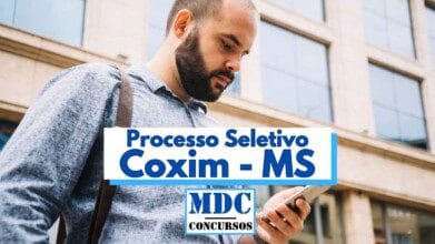Processos Seletivos 3 Homem barbudo e calvo, vestindo camisa azul clara e mochila, está concentrado olhando para seu celular em uma área urbana com prédio de janelas espelhadas ao fundo. No centro da imagem, há uma faixa com os dizeres "Processo Seletivo Coxim - MS" em letras grandes e azuis. Abaixo, aparece o logotipo do portal MDC Concursos. A imagem transmite foco e atenção à informação.