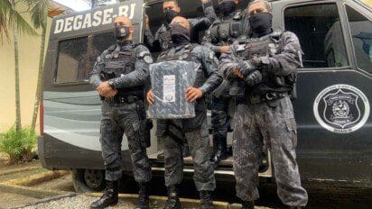 Agentes uniformizados do DEGASE-RJ posam em frente a viatura oficial com armamento e equipamento de proteção.