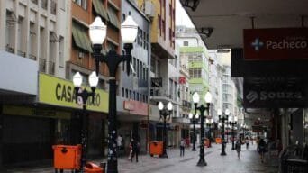Calçadão comercial em Juiz de Fora com postes de luz antigos, lojas fechadas e algumas pessoas caminhando durante o dia.