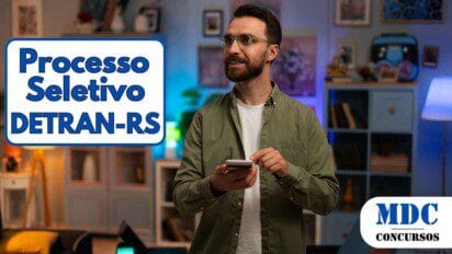 Homem com barba e óculos segura um celular e sorri em uma sala iluminada com luzes coloridas, rodeado por estantes, quadros e móveis modernos - DETRAN RS oferece 28 vagas e salários de até R$ 10,8 mil em Processo Seletivo