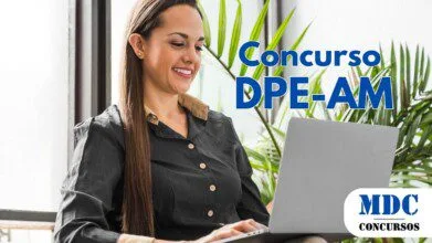 Mulher de cabelos longos e castanhos, vestindo camisa preta com detalhes bege, sorrindo enquanto usa um laptop prateado. Ela está sentada em uma cadeira confortável, cercada por plantas verdes, perto de uma janela com luz natural - DPE AM abre Concurso com remuneração de R$ 19.134